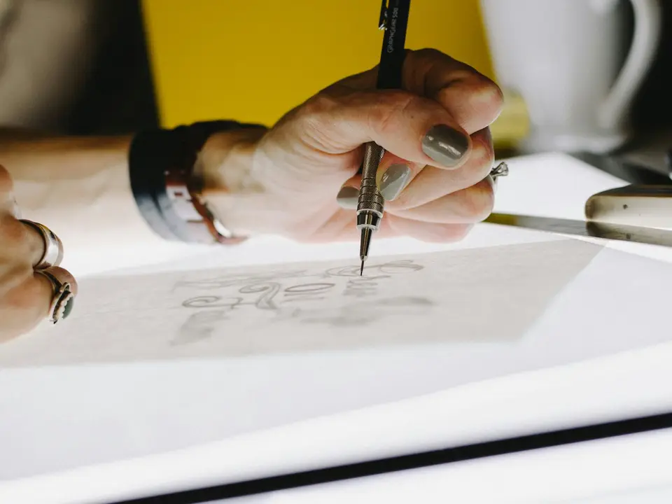 A hand lettering a word on tracing paper with a pencil