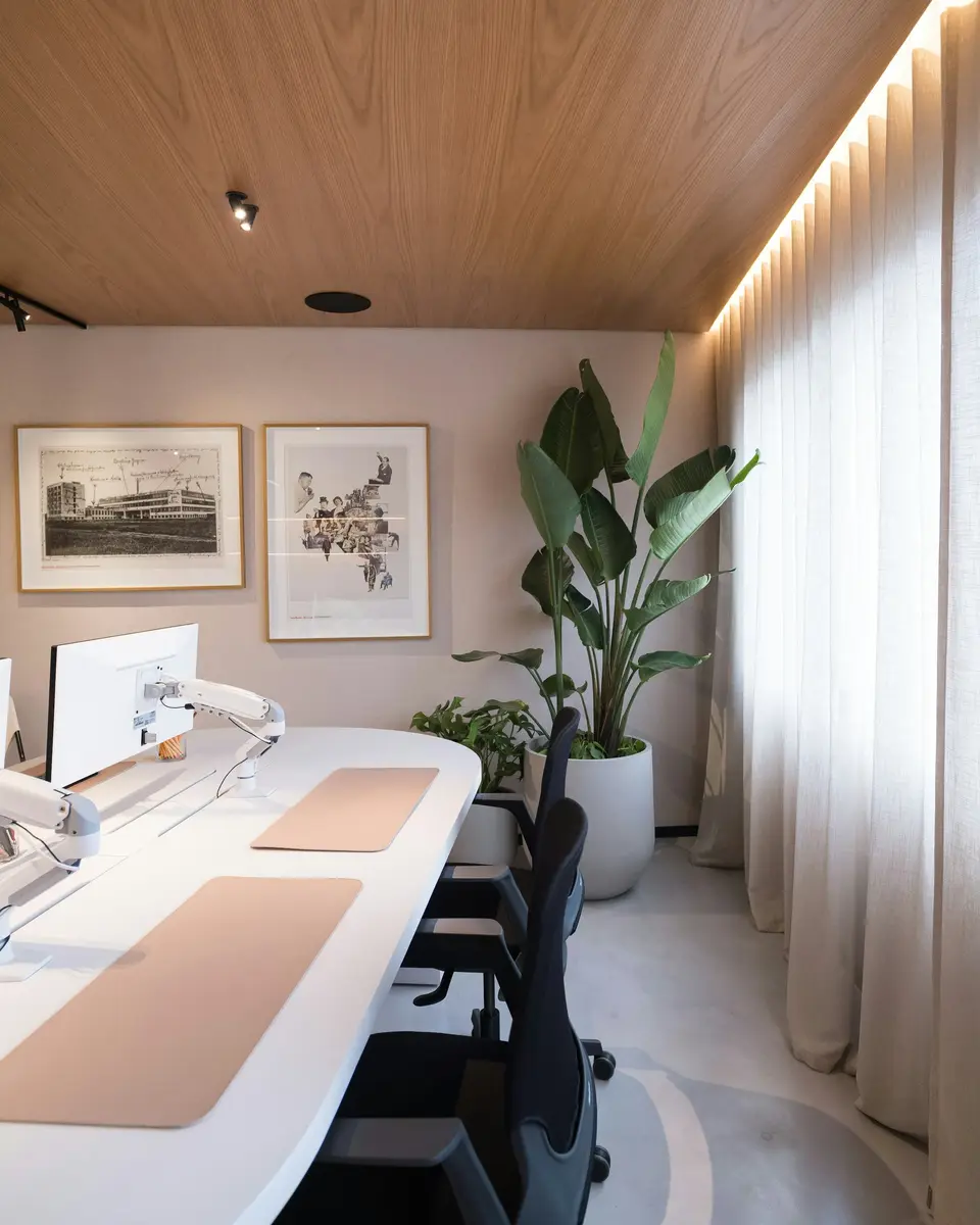 The studio: long white desks, plants and framed prints under a wooden ceiling